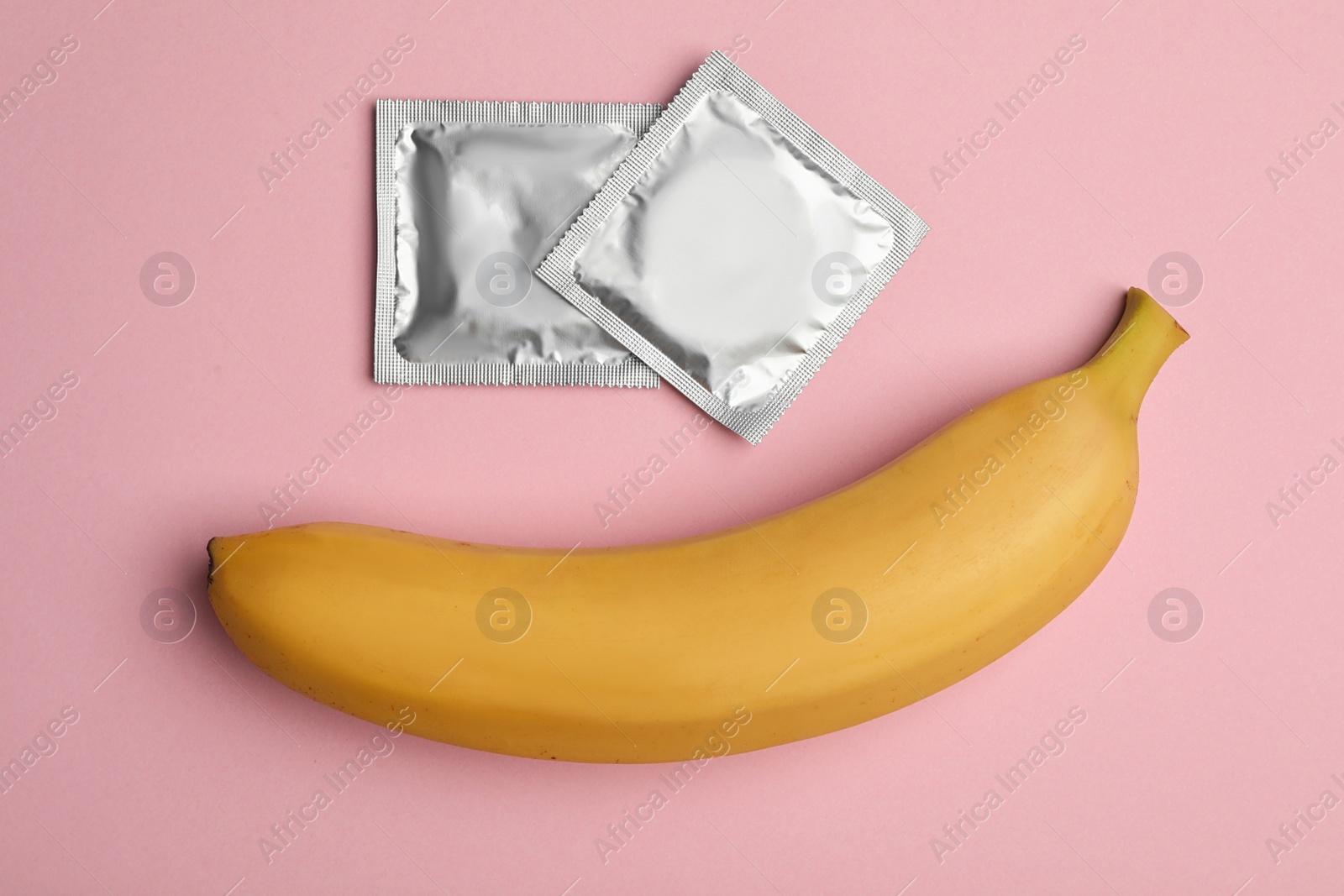 Photo of Condoms with banana on pink background, flat lay. Safe sex