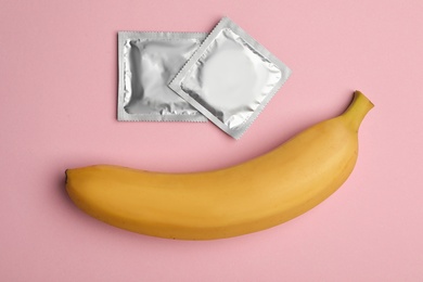 Photo of Condoms with banana on pink background, flat lay. Safe sex