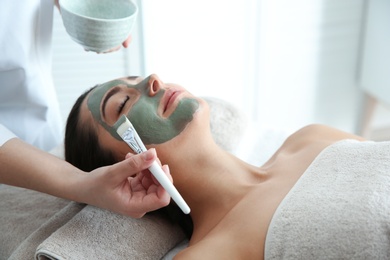 Photo of Cosmetologist applying mask on client's face in spa salon