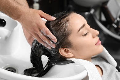 Stylist washing client's hair at sink in beauty salon