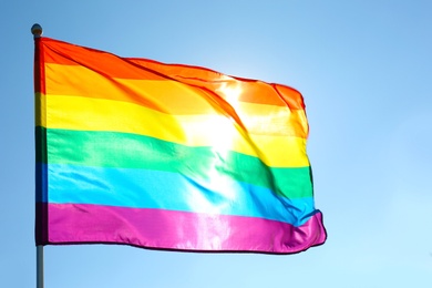 Photo of Rainbow LGBT flag fluttering on blue sky background. Gay rights movement