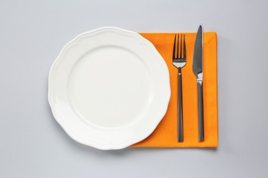 Photo of Clean plate and shiny silver cutlery on light grey background, flat lay