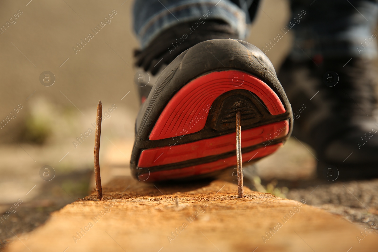 Photo of Careless worker stepping on nail in wooden plank outdoors, closeup