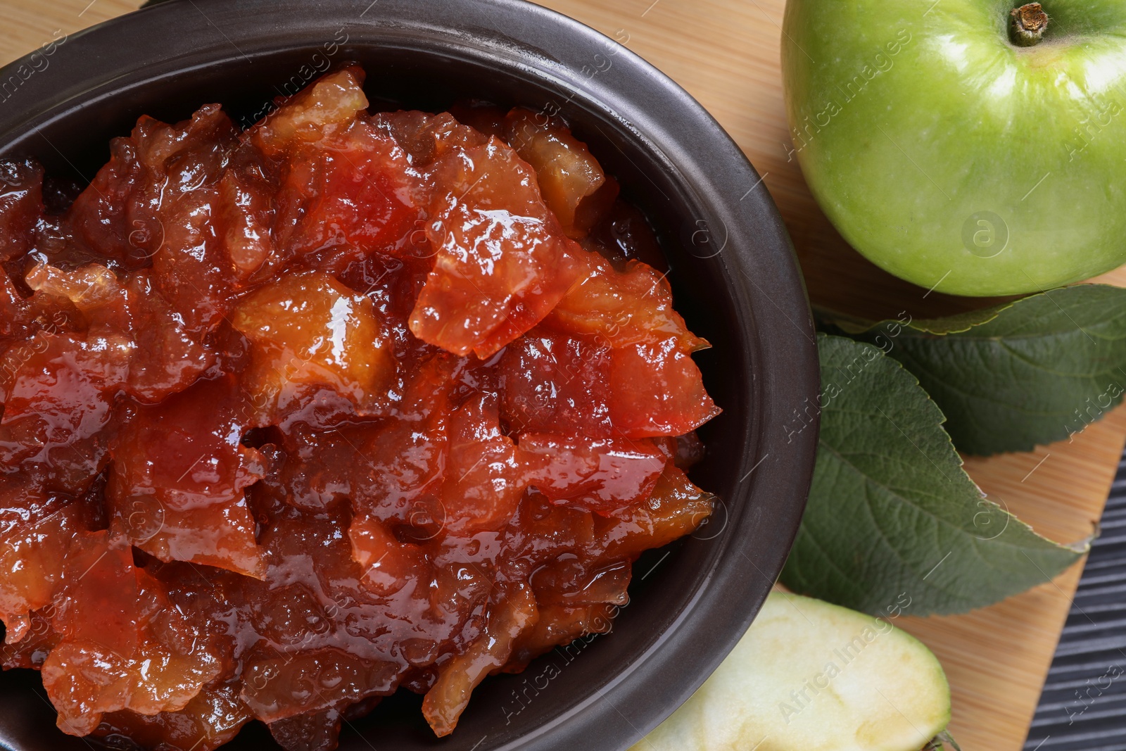 Photo of Bowl of delicious apple jam and fresh fruits on black wooden table, flat lay