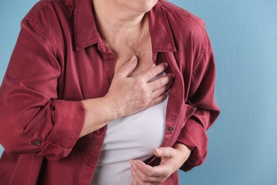 Mature woman having heart attack on color background