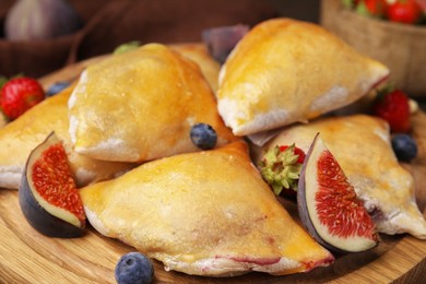 Photo of Delicious samosas with figs and berries on wooden board, closeup