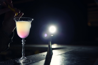 Photo of Barman adding lemon zest into cosmopolitan martini cocktail at counter, closeup. Space for text