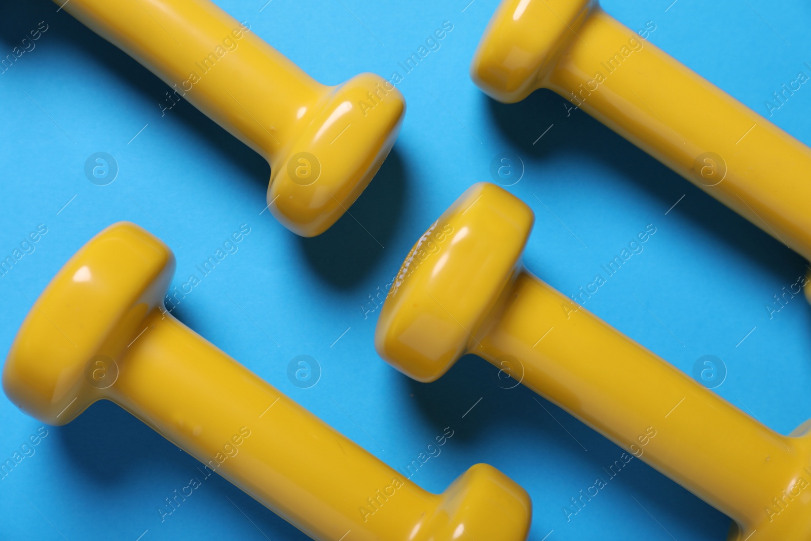 Photo of Yellow dumbbells on light blue background, flat lay. Morning exercise