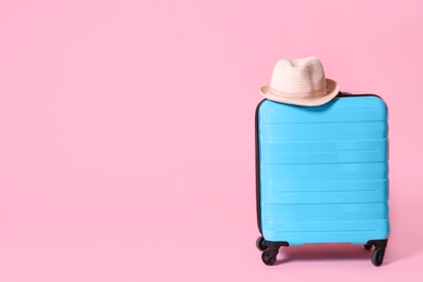 Photo of Modern blue suitcase and hat on light pink background. Space for text
