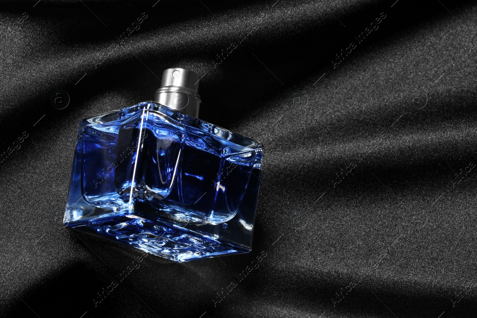 Photo of Luxury men's perfume in bottle on black satin fabric, above view. Space for text