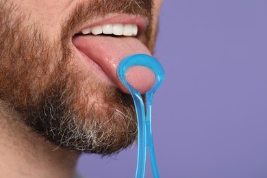 Man brushing his tongue with cleaner on violet background, closeup. Space for text