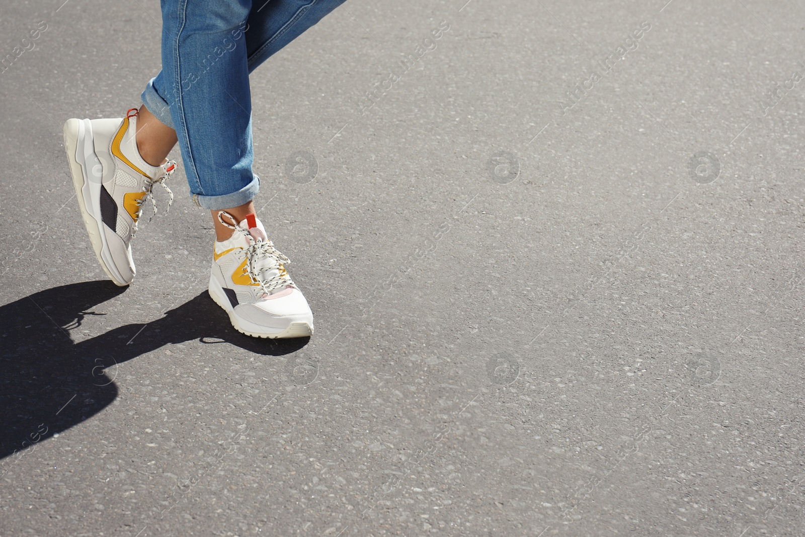 Photo of Woman in stylish sneakers walking outdoors, focus on legs. Space for design