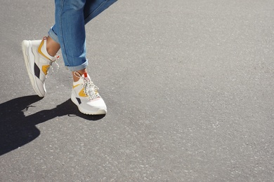 Woman in stylish sneakers walking outdoors, focus on legs. Space for design