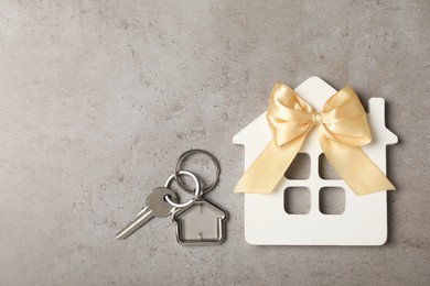 Photo of Wooden house model, bow and key on grey table, flat lay with space for text. Housewarming party