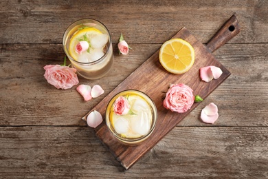 Photo of Delicious refreshing drink with lemon and roses on wooden table, flat lay