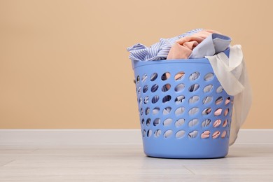 Photo of Laundry basket with clothes near beige wall indoors. Space for text