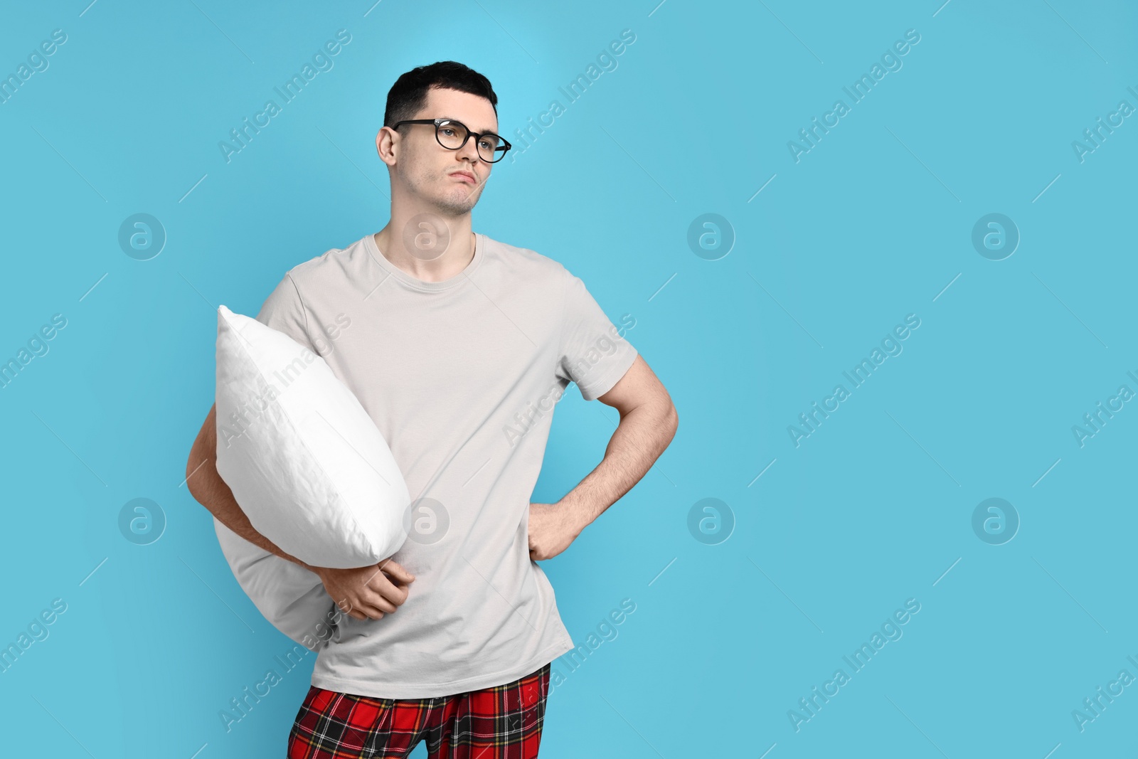 Photo of Man in pyjama holding pillow on light blue background, space for text