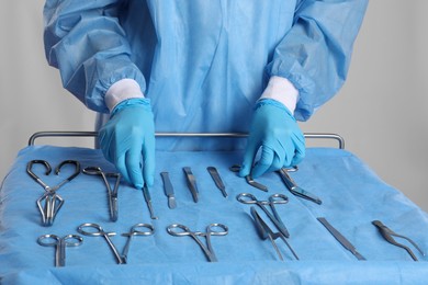 Photo of Doctor taking surgical instruments from table on light background, closeup