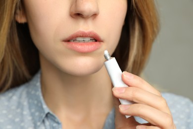 Photo of Woman with herpes applying cream onto lip against light grey background, closeup