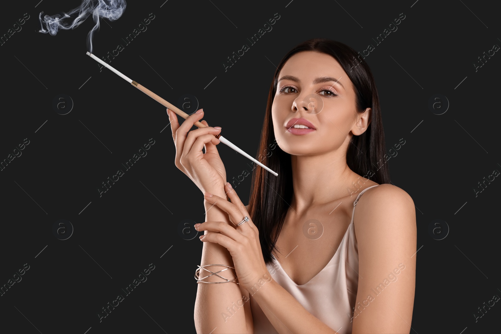 Photo of Woman using long cigarette holder for smoking on black background