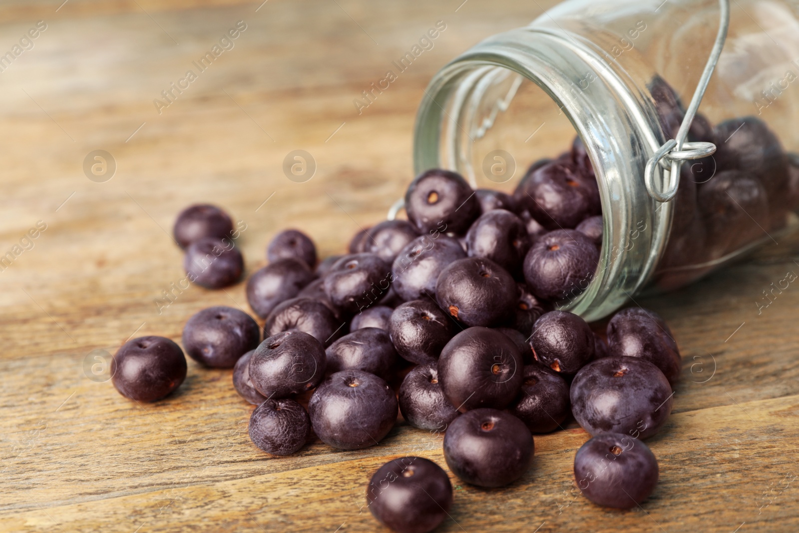 Photo of Fresh acai berries scattered from jar on wooden table, closeup view. Space for text