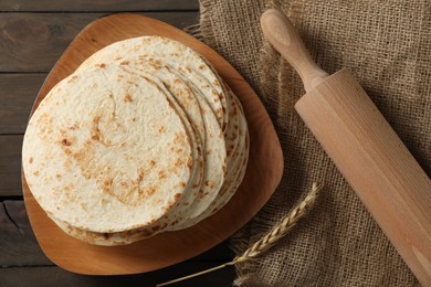 Many tasty homemade tortillas and rolling pin on wooden table, top view