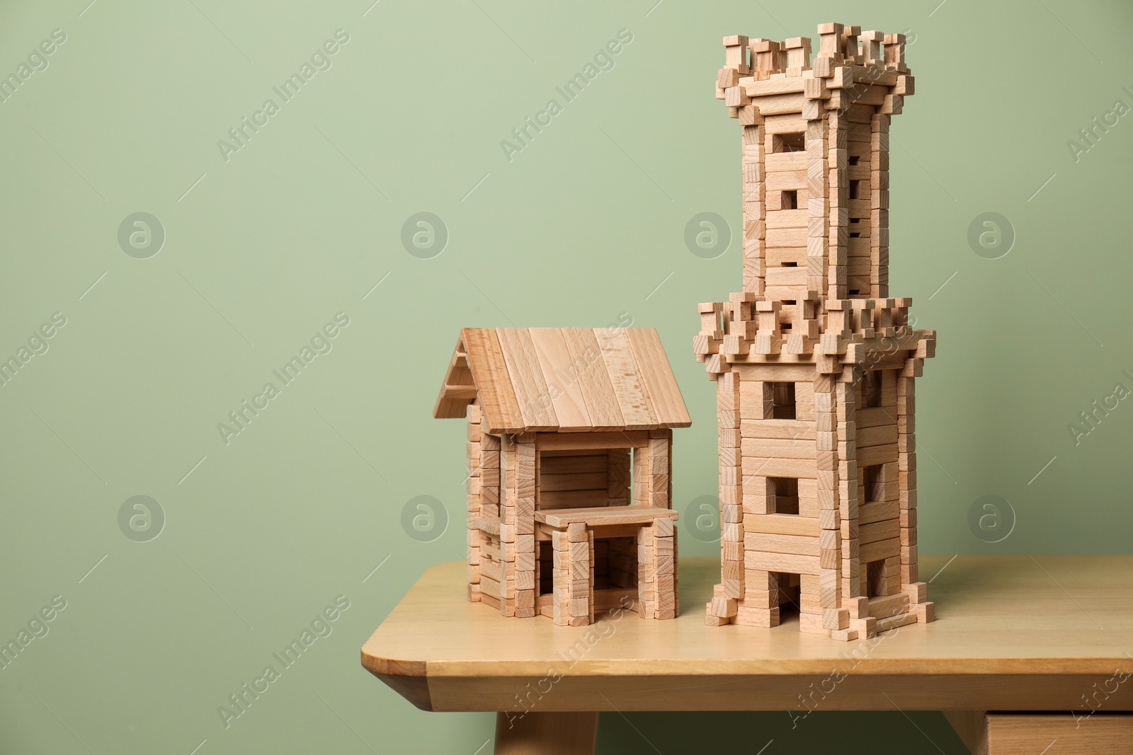 Photo of Wooden tower and house on table near olive wall, space for text. Children's toys