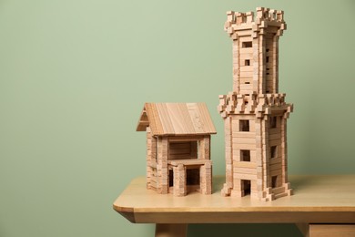 Wooden tower and house on table near olive wall, space for text. Children's toys