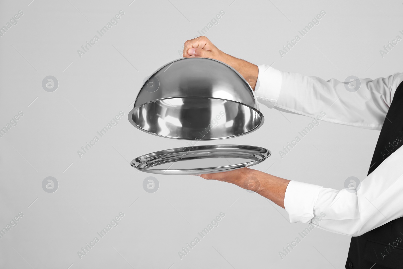 Photo of Waiter holding metal tray with lid on grey background