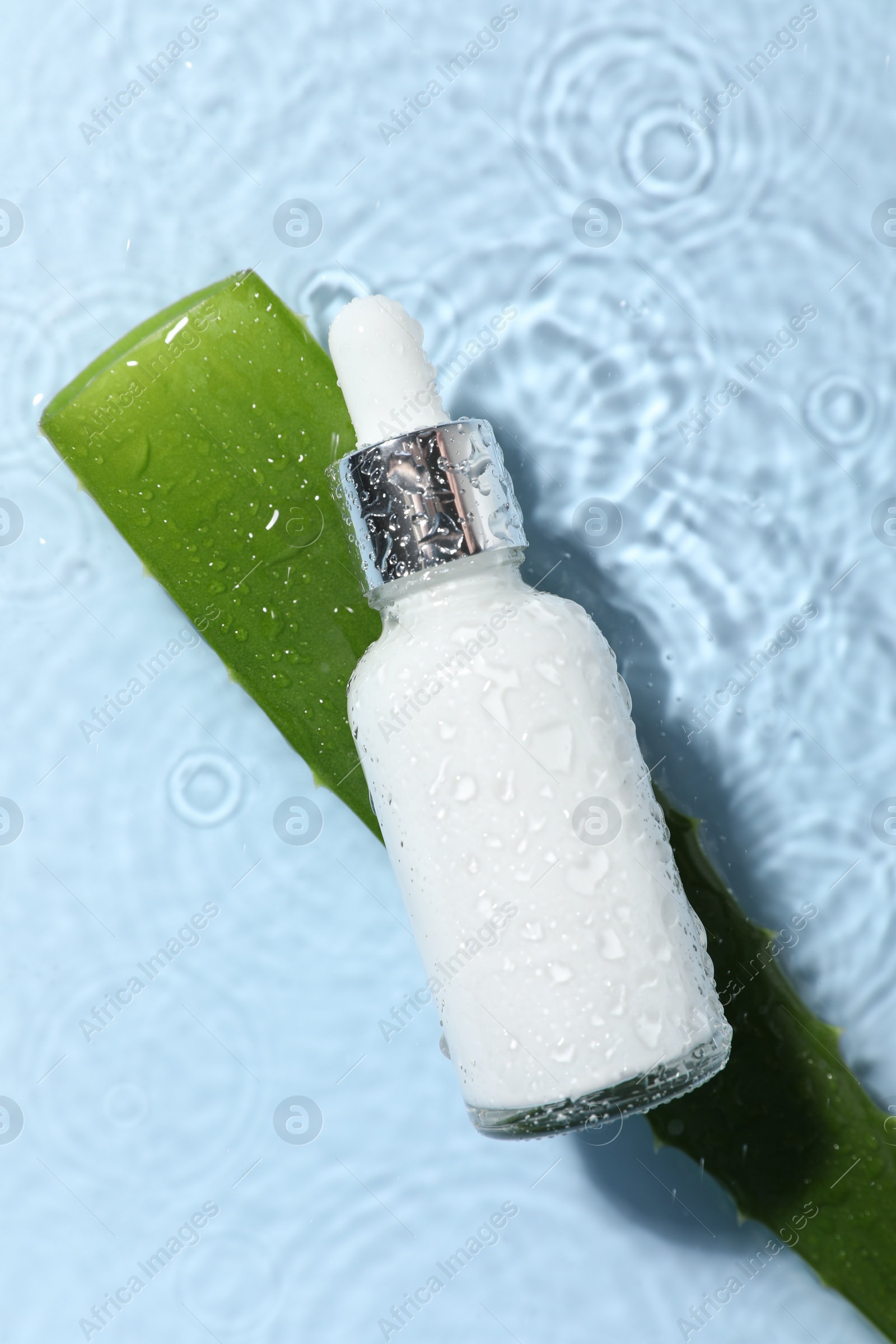 Photo of Bottle of cosmetic product and aloe leaf in water on light blue background, flat lay