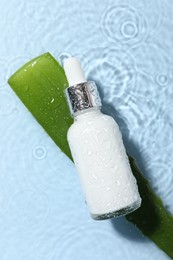 Photo of Bottle of cosmetic product and aloe leaf in water on light blue background, flat lay