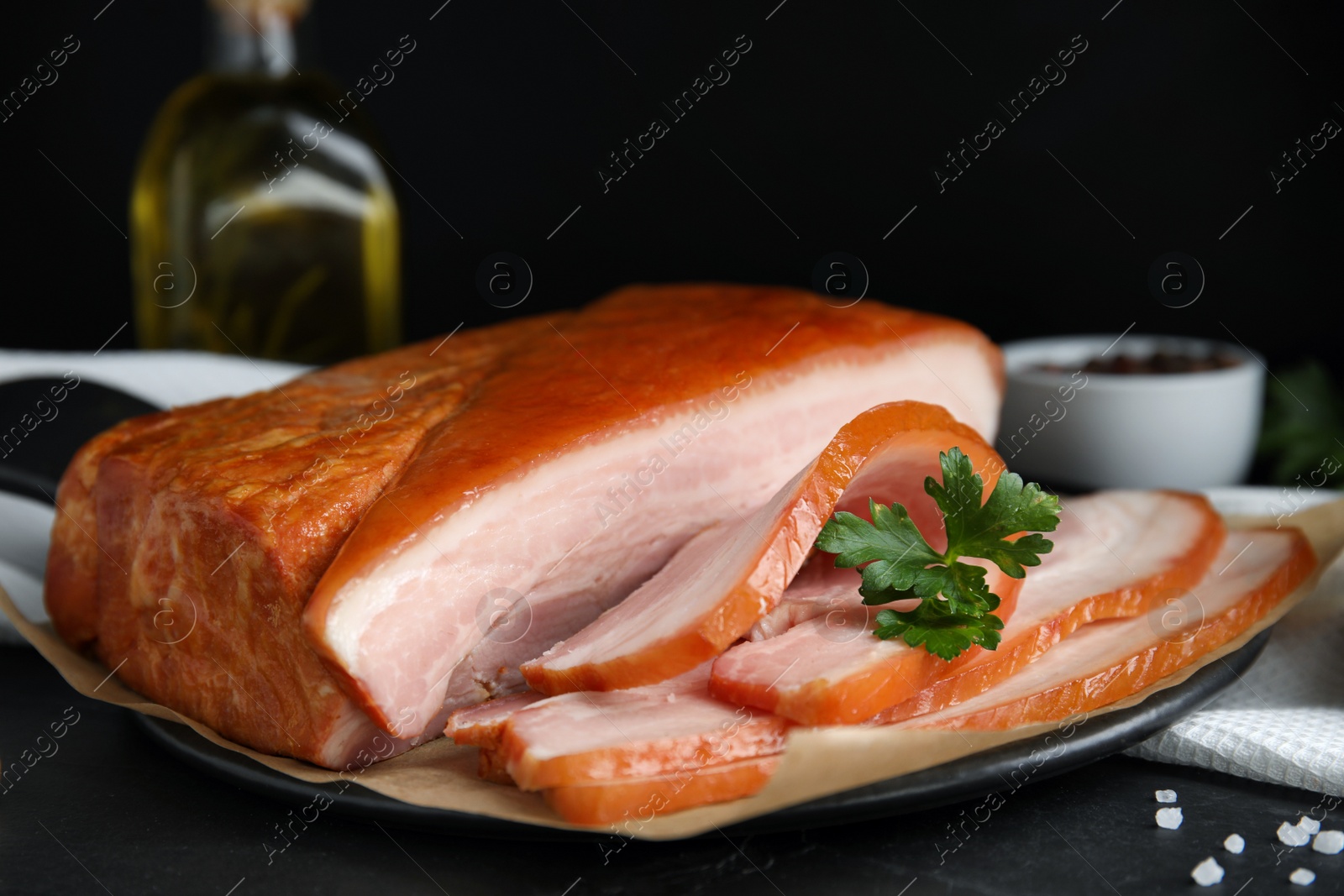 Photo of Delicious smoked bacon with parsley and salt on black table, closeup