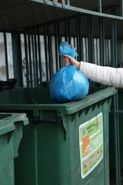 Photo of Woman throwing trash bag full of garbage in bin outdoors, closeup