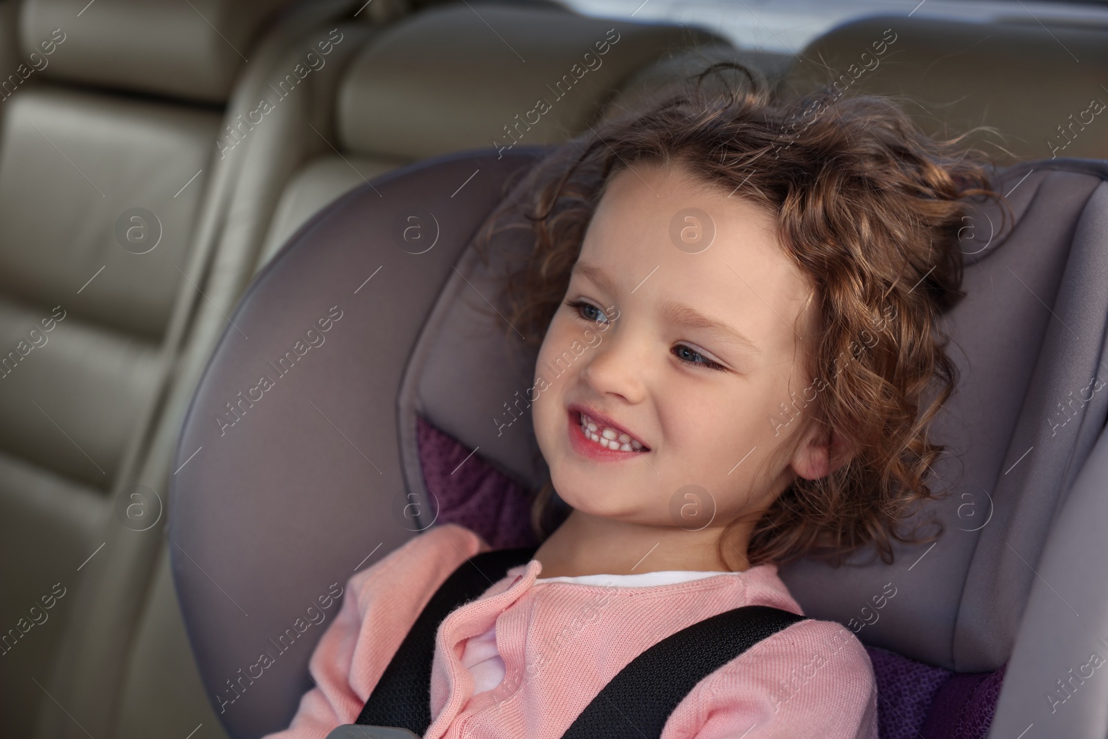 Photo of Cute little girl sitting in child safety seat inside car