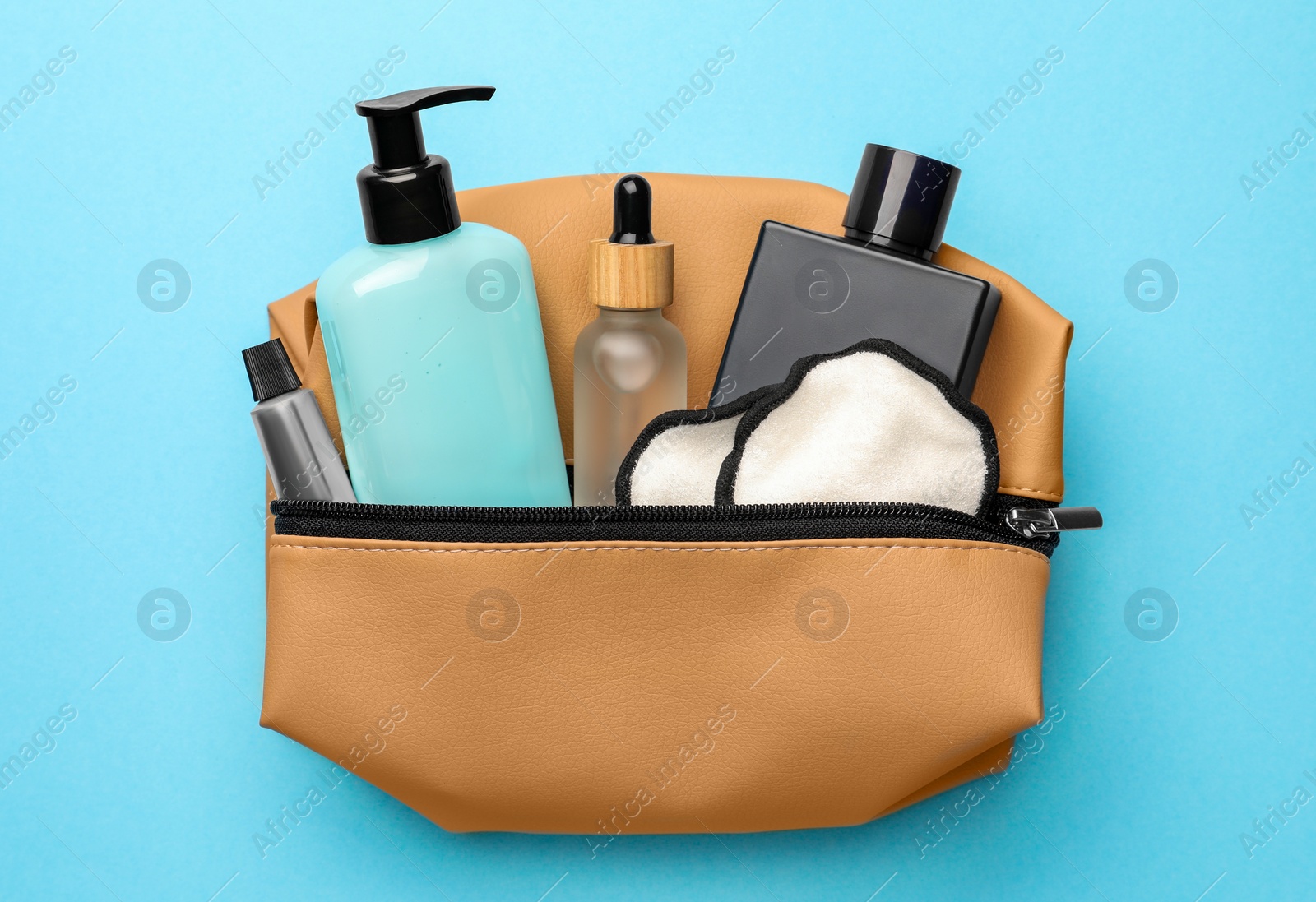 Photo of Preparation for spa. Compact toiletry bag with different cosmetic products on light blue background, top view