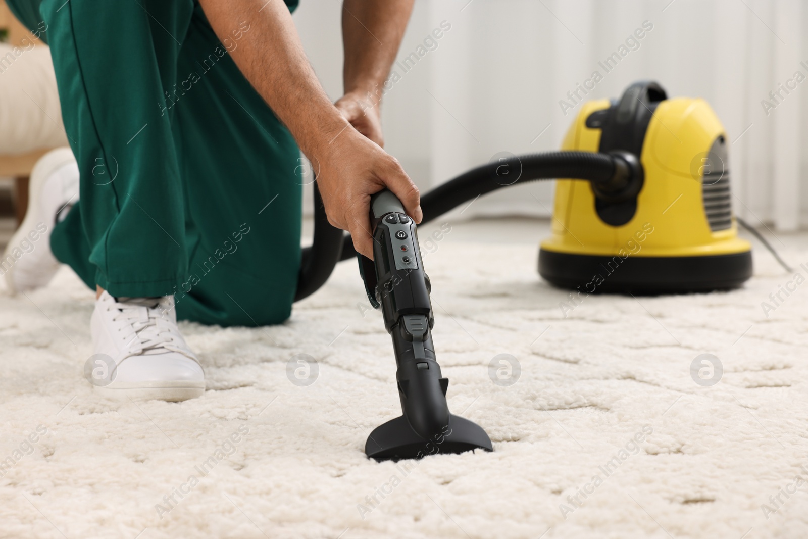 Photo of Dry cleaner's employee hoovering carpet with vacuum cleaner indoors, closeup