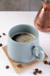 Delicious coffee in cup and beans on white textured table, closeup