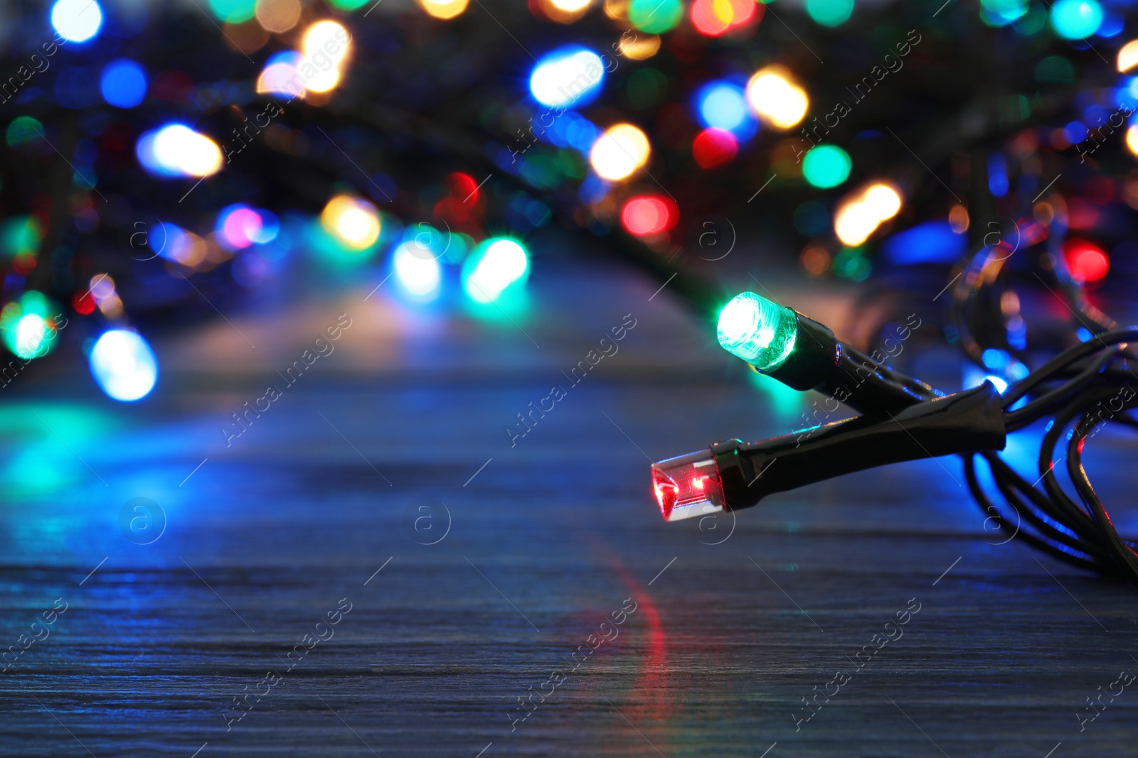 Photo of Glowing Christmas lights on wooden table, closeup