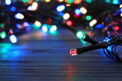 Photo of Glowing Christmas lights on wooden table, closeup