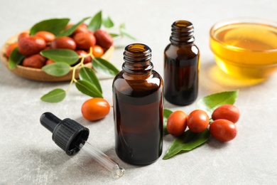 Photo of Glass bottle with jojoba oil and seeds on grey stone table