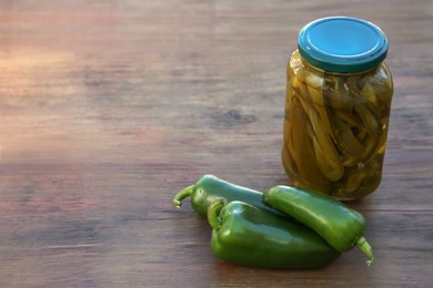 Photo of Fresh and pickled green jalapeno peppers on wooden table. Space for text