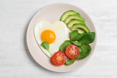 Photo of Plate of tasty breakfast with heart shaped fried egg on white wooden table, top view