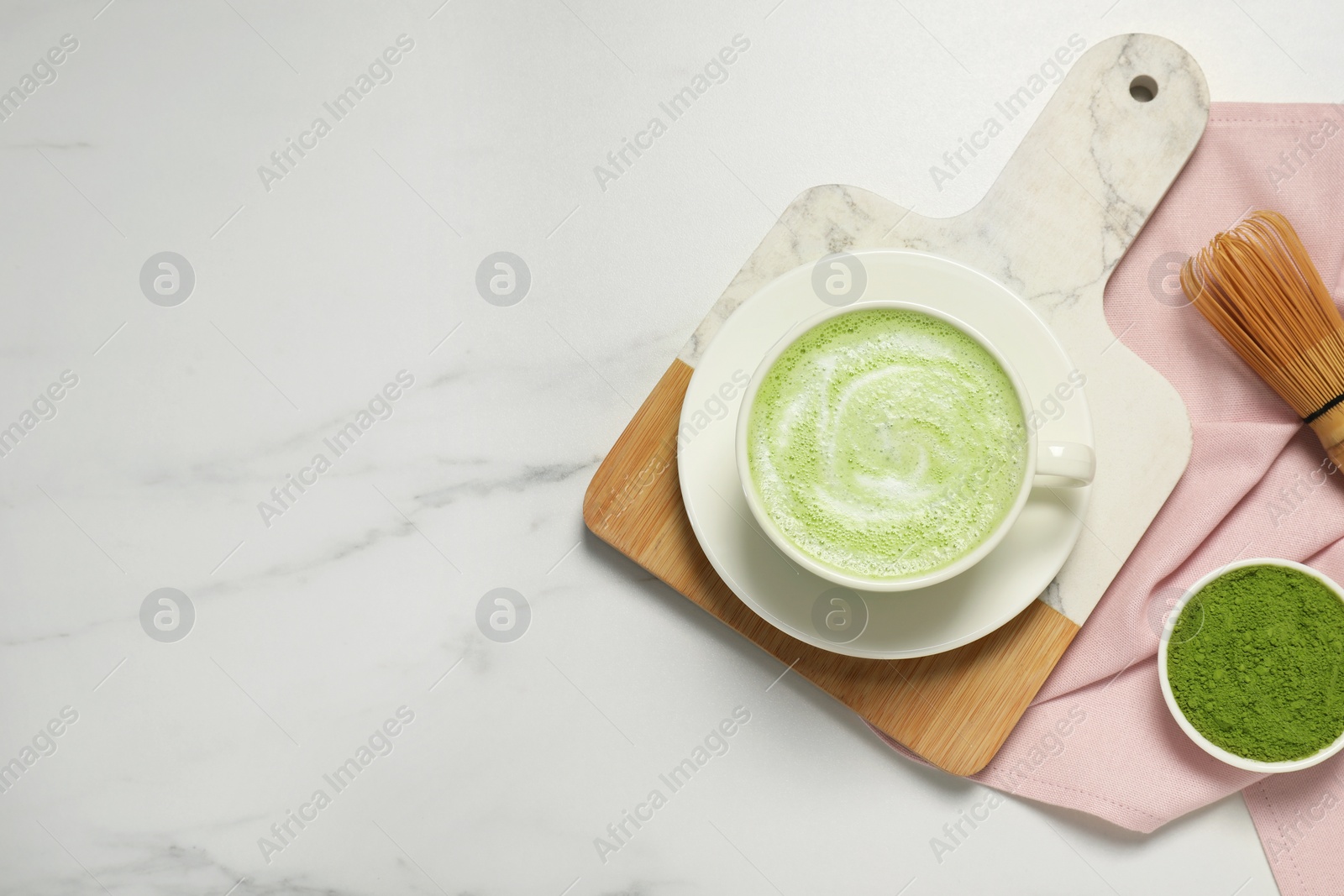 Photo of Cup of fresh matcha latte and powder on white marble table, flat lay. Space for text