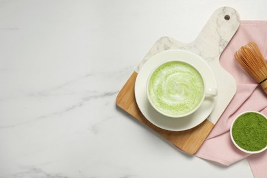 Cup of fresh matcha latte and powder on white marble table, flat lay. Space for text