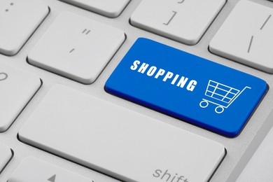 Image of Online store purchase. Blue button with word Shopping and cart on laptop, closeup