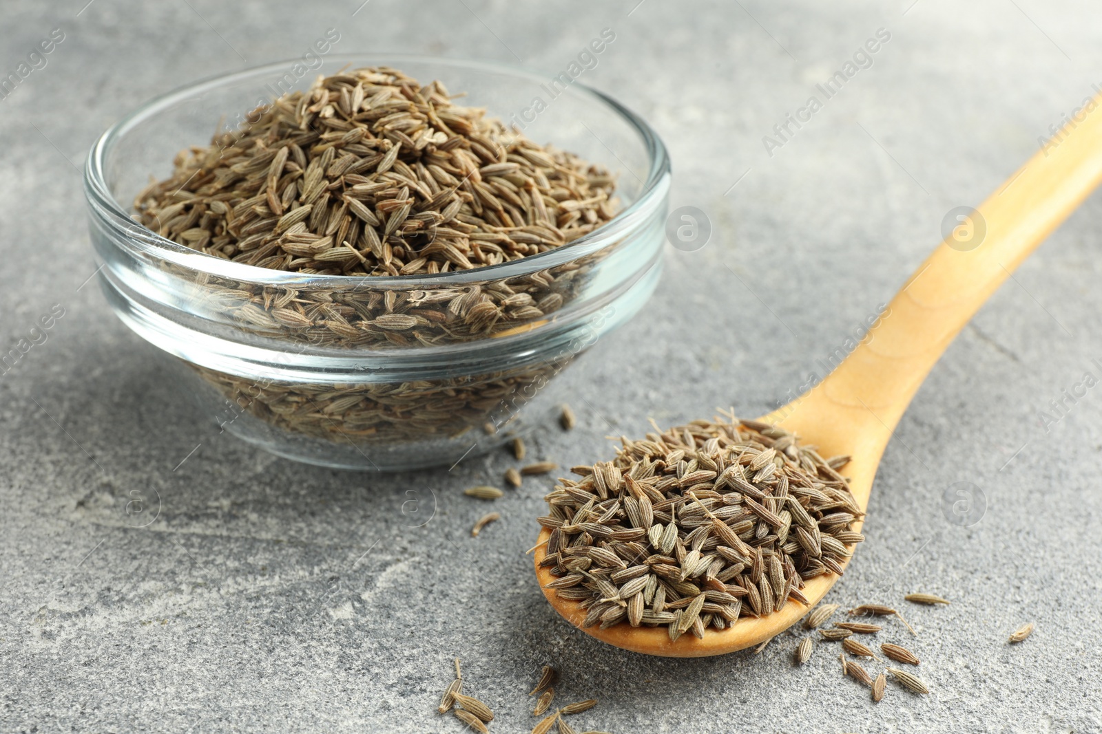 Photo of Bowl of caraway seeds and spoon on grey table, closeup