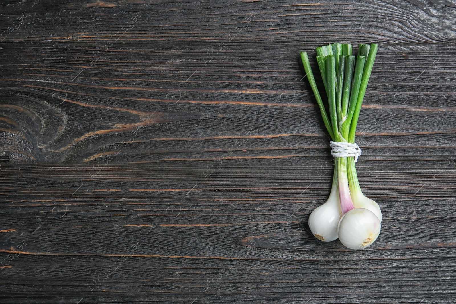 Photo of Tied fresh green onion on wooden table, top view