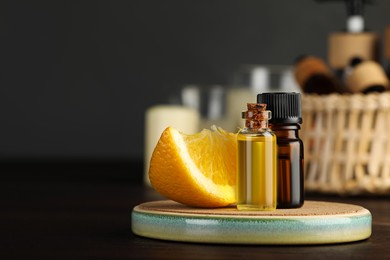 Photo of Bottles of essential oil and orange on wooden table, space for text