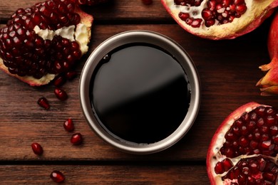 Photo of Glass bowl of tasty pomegranate sauce and fresh ripe fruit on wooden table, flat lay