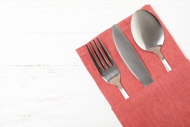 Photo of Folded napkin with fork, spoon and knife on white wooden background, top view. Space for text